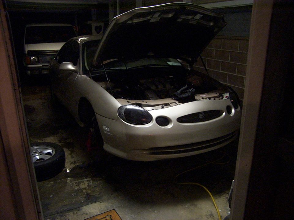 Silver sedan with hood open, front view, parked in garage next to a white van