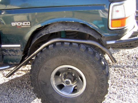 1995 Ford Bronco - Close-up of a green SUV's fender and off-road tire, a visible 'Bronco' badge and custom roll cage.