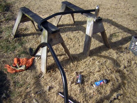 1995 Ford Bronco - Black metal bars are supported by sawhorses outdoors, with spray paint cans and a rag nearby.