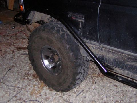 1995 Ford Bronco - Close-up of the front wheel and fender of a black Ford Bronco XLT, showing its off-road tires and side protection.