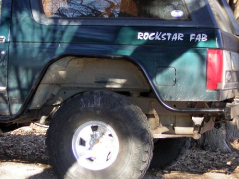 1995 Ford Bronco - The rear section of a green SUV shows off-road modifications and a custom decal on the body panel.