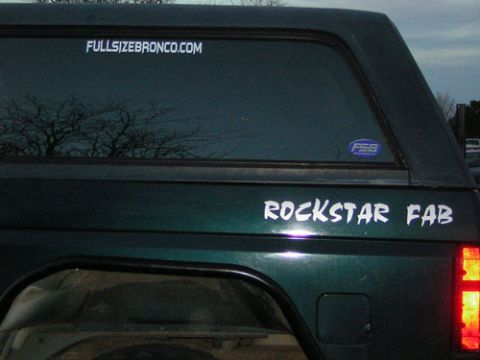 1995 Ford Bronco - The rear of a dark green Ford Bronco shows custom decals on the body and window.