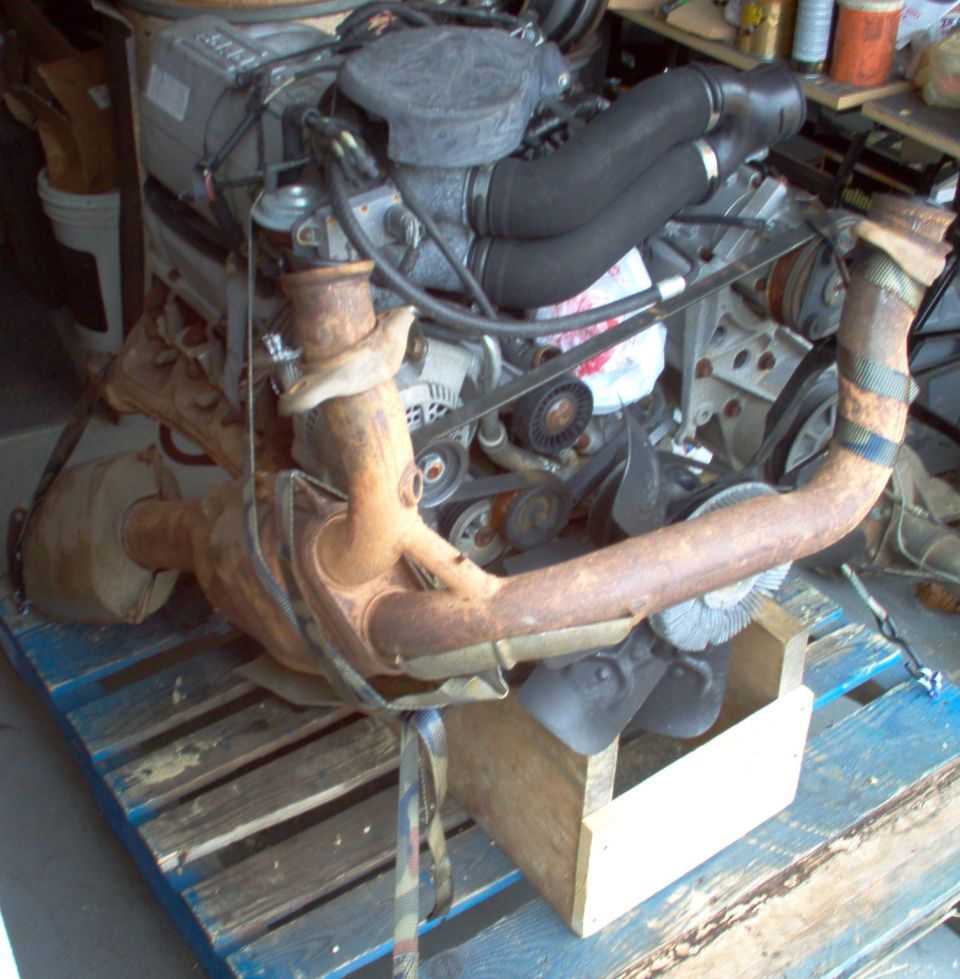 V8 engine showing exhaust crossover and fan clutch resting on a pallet