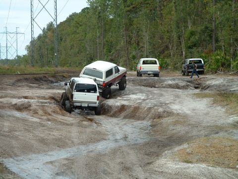 1995 Ford Bronco - Multiple SUVs navigate a challenging off-road course with muddy ruts and uneven terrain.