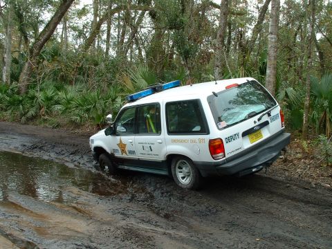 1995 Ford Bronco - A white Ford Explorer SUV, marked as a deputy vehicle, is stuck in the mud on a dirt road.