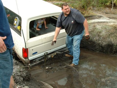 1995 Ford Bronco - A white Ford Bronco is stuck in the mud with people trying to get it out.
