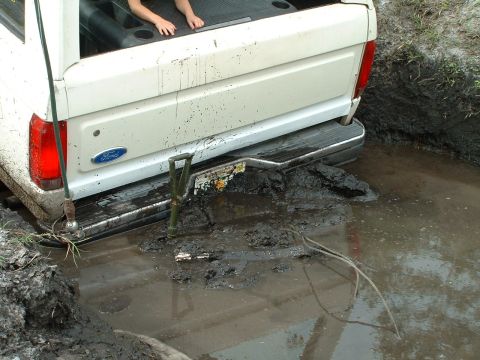 1995 Ford Bronco - A white Ford pickup truck is stuck in deep mud, with its rear end partially submerged.