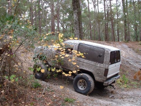 1995 Ford Bronco - Mud-covered 1995 Ford Bronco navigating a dirt path in a forest.