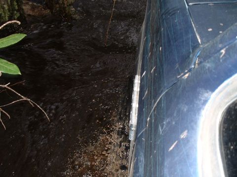 1995 Ford Bronco - A blue SUV navigates through dark, murky water, its side panel showing numerous scratches.