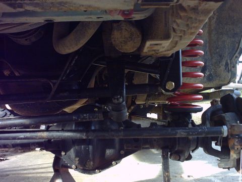 1995 Ford Bronco - Close-up view of the undercarriage suspension system, showing the front axle and red coil springs.