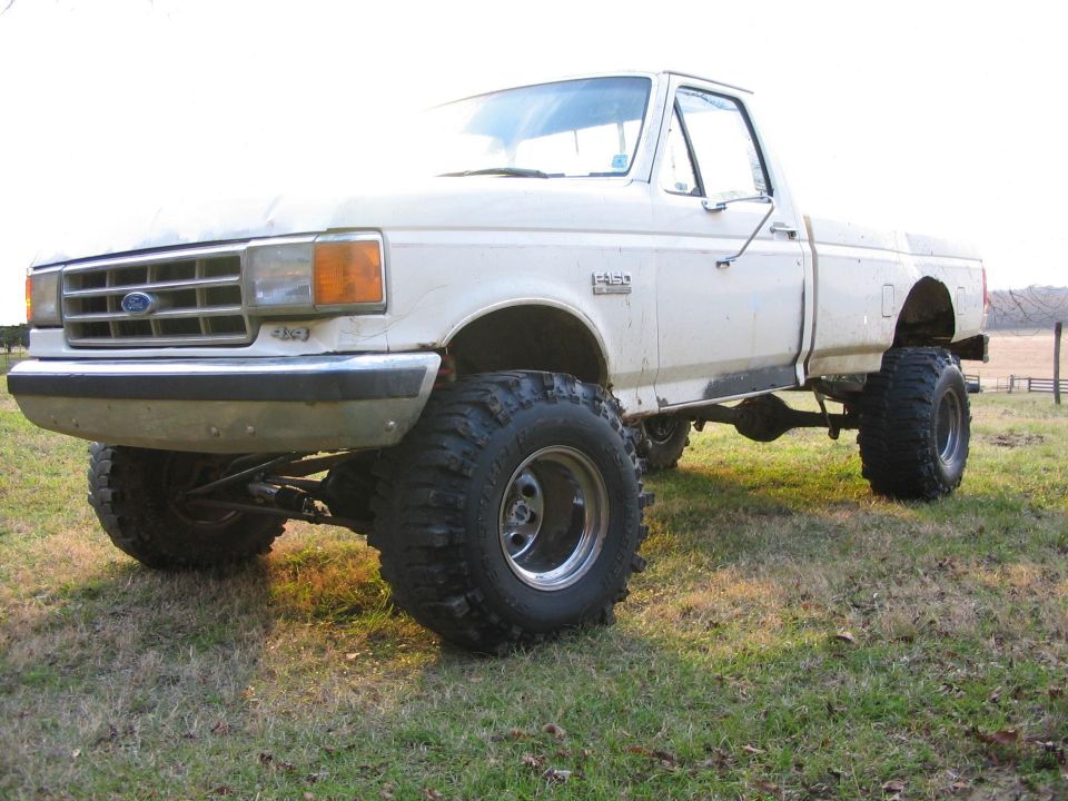 White lifted 1987-1991 Ford F-series 4x4 pickup on mud tires in field