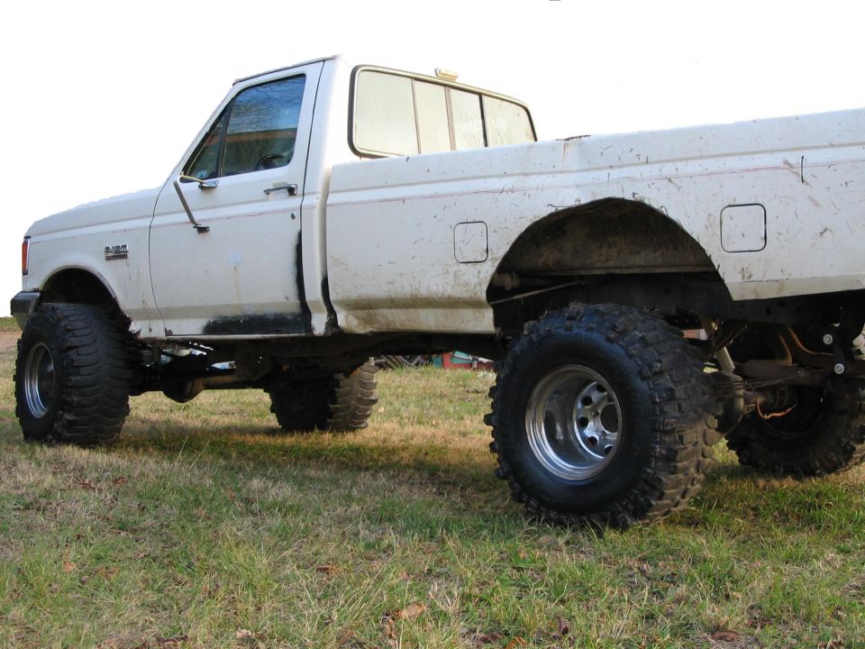 White lifted Ford F-150 pickup on mud tires parked in a grassy field
