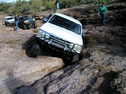 1993 Ford Bronco - Several off-road vehicles are navigating a challenging rocky trail in a desert environment.