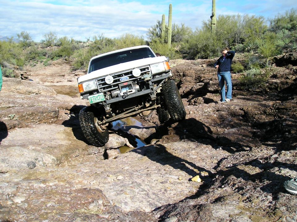 White lifted Ford Bronco with winch bumper flexing over desert rock ledge