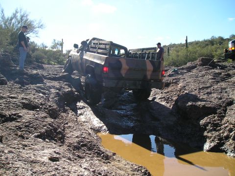 1993 Ford Bronco - A camouflaged pickup truck navigates a challenging muddy and rocky off-road course.