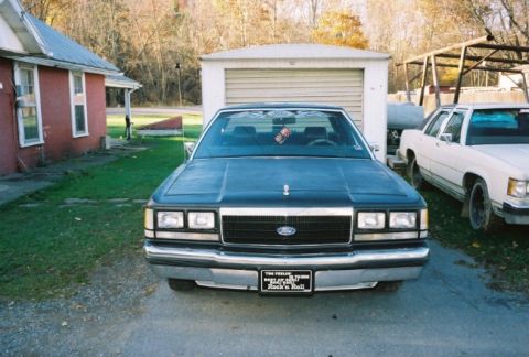1989 Ford Crown Victoria LTD - A dark blue Ford Crown Victoria is parked in front of a garage, with another white car to its right.