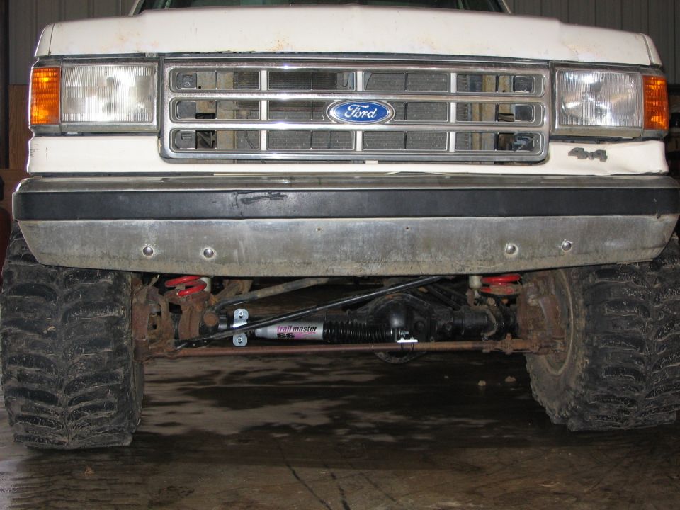 Front of white lifted Ford 4x4 pickup showing solid axle, mud tires, and Trail Master SS steering stabilizer