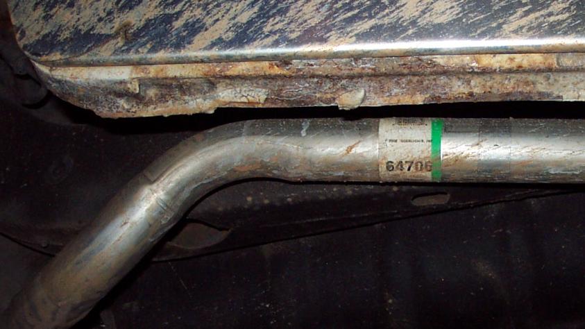 Undercarriage view of a rusted metal panel above an exhaust pipe with a label showing '64706'