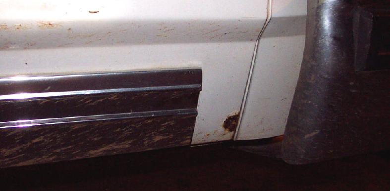 White car door bottom with chrome trim, mud, and rust spot
