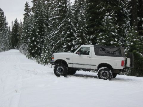 1995 Ford Bronco - A white 1995 Ford Bronco with a soft top navigates a snowy forest road.