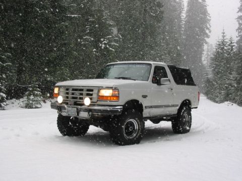 1995 Ford Bronco - A 1995 Ford Bronco navigates a snow-covered road in a wooded area during a snowfall.