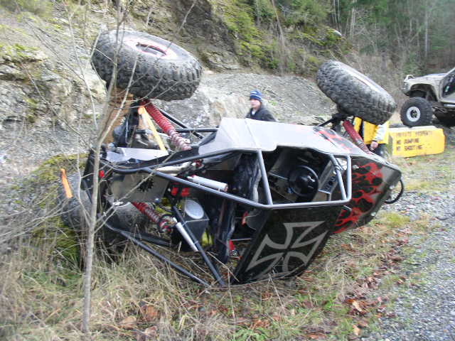 Overturned off-road buggy with large tires, another vehicle visible in background