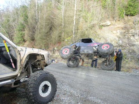 1978 Ford Bronco - Two off-road vehicles are on a dirt road with trees and rocks in the background. People are attending to the buggy.