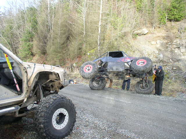 Silver tube-chassis rock buggy on a gravel road beside a tan lifted Jeep