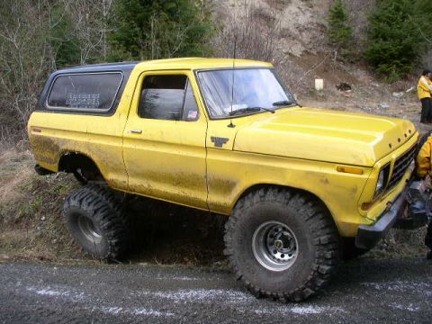 1978 Ford Bronco - A yellow 1978 Ford Bronco is parked on the side of a dirt road with large off-road tires.