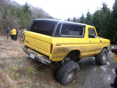 1978 Ford Bronco - Mud-splattered yellow full-size Ford Bronco with a black removable hardtop, shot from the 3/4 rear as it sits with one rear wheel dropped o…