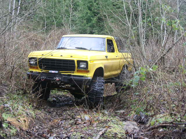 Yellow topless lifted Ford Bronco with winch bumper on a muddy wooded trail