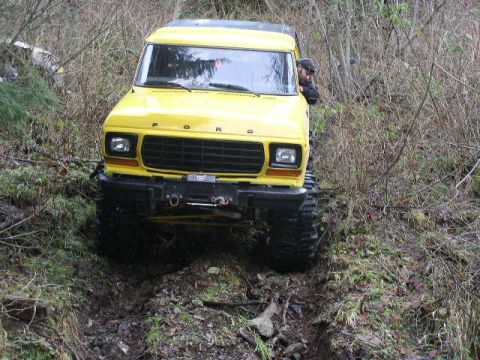 1978 Ford Bronco - Head-on view of a yellow lifted full-size Ford Bronco with a black hardtop working down a narrow, rocky washout in the brush. The front win…