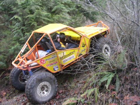 1978 Ford Bronco - Side view of a yellow chopped-cab rock crawler with a full orange exterior roll cage and BFGoodrich, Beadlock and Sedona sponsor decals, cl…