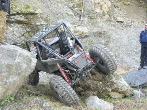 1978 Ford Bronco - Grey tube-chassis rock buggy flexed hard over boulders in a rocky quarry, articulating with one front tire stuffed and a rear tire hanging…