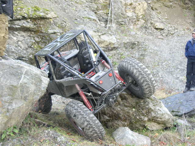Grey tube-chassis rock buggy flexed over boulders in a rocky quarry