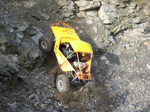 1978 Ford Bronco - Overhead view looking down on a yellow rock buggy with an orange exterior roll cage as it climbs a steep rock quarry wall, nose down in the…