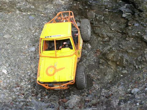 1978 Ford Bronco - Overhead view of a chopped yellow rock crawler with a full orange exterior roll cage and sponsor decals including 'XXX Traction', working a…