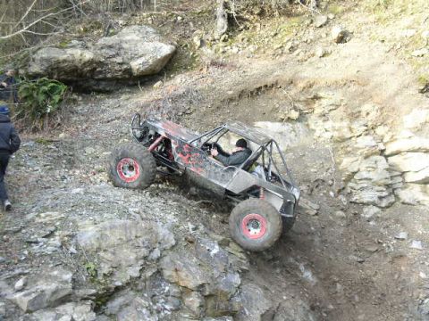 1978 Ford Bronco - A tube-chassis rock buggy with bare aluminum panels, red graphics and red-centered wheels crawls down a rocky ledge on a dirt trail, driver…