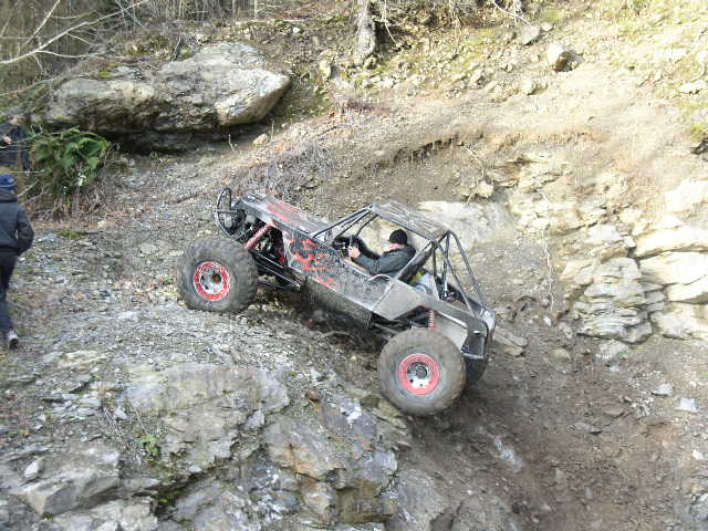 Tube-chassis rock buggy with red wheels crawling down a rocky ledge