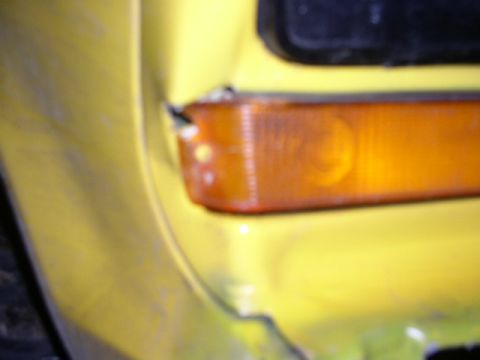 1978 Ford Bronco - Blurry close-up of an amber rectangular turn signal / parking lamp lens set into a yellow front body panel beside the dark grille opening.…