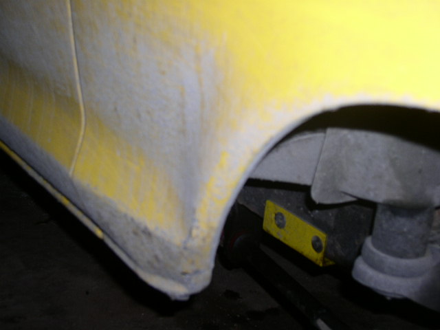 Yellow wheel arch sanded to primer with wheel removed showing leaf spring