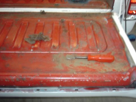 1978 Ford Bronco - Interior of a red truck bed shows a screwdriver and debris, suggesting preparation for a bedliner application.