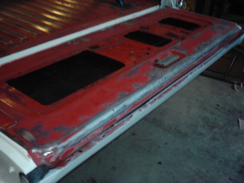 1978 Ford Bronco - The tailgate of a truck is shown with red paint, black inserts, and areas of rust and primer.