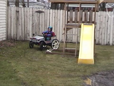 1985 Ford F-150 - A child enjoys a ride in a toy jeep in the backyard beside a wooden playset with a yellow slide.