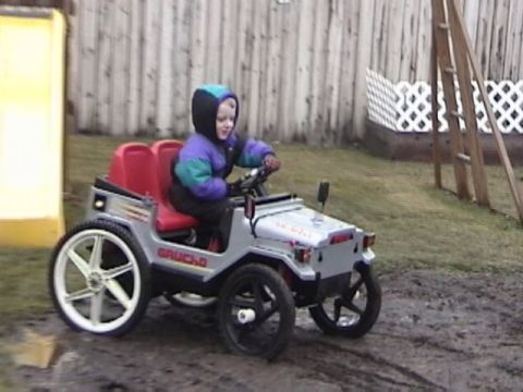 1985 Ford F-150 - A child drives a silver toy jeep with red seats in a backyard setting.