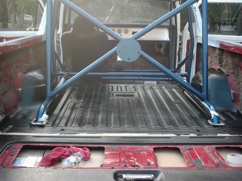 1978 Ford Bronco - The interior of a truck bed is visible, modified with a blue roll cage and a black bedliner.