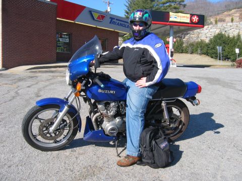 1985 Ford Crown Victoria LTD - A rider sits on a blue Suzuki motorcycle parked at a Triangle gas station.