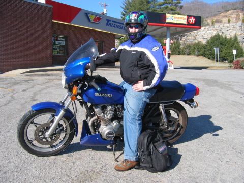 1985 Ford Crown Victoria LTD - A rider pauses at a Triangle Gas station with a blue Suzuki motorcycle.