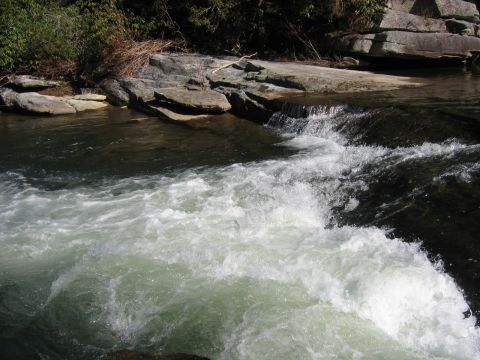 1985 Ford Crown Victoria LTD - A scenic view of whitewater rapids flowing over rocks, surrounded by trees and boulders.