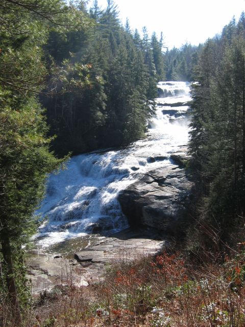 1985 Ford Crown Victoria LTD - A wide waterfall flows down a rocky incline surrounded by dense evergreen trees.
